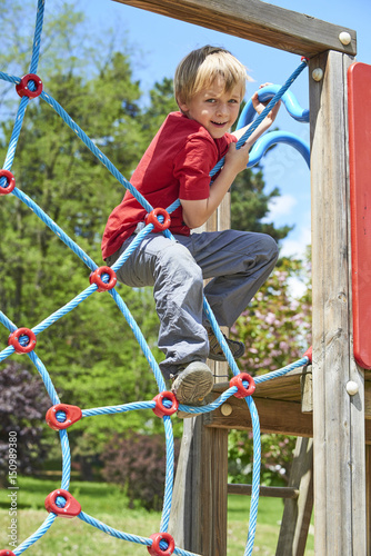 Child boy climbing rope web on the children playground outdoors at summer