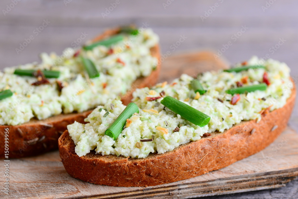 Rye bread toast with guacamole, fresh green onion and spices on a wooden board. Nutritious toast idea for a picnic, breakfast or lunch. Home avocado recipe. Closeup