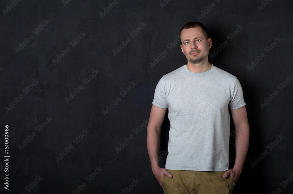 Portrait of a nice guy in casual clothes. An attractive guy leaning on a black wall keeps his hands in his pockets. Portrait of a nice guy in casual clothes. An attractive guy leaning on a black wall keeps his hands in his pockets.