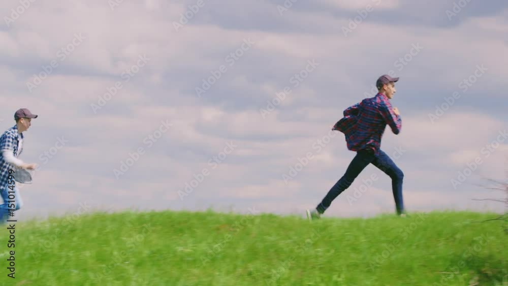 Two teenage boys bang one after another over a beautiful green hill against a blue sky with clouds Two teenage boys bang one after another over a beautiful green hill against a blue sky with clouds