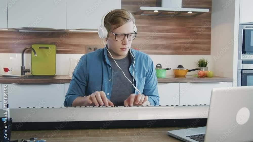 Young man learning synthesizer watching at online lessons on laptop computer