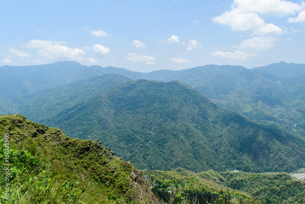 A hilltop view of mountains and blue sky with clouds  on a misty day.