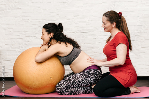 Midwife massaging a pregnant woman while exercising with a fitness ball photo