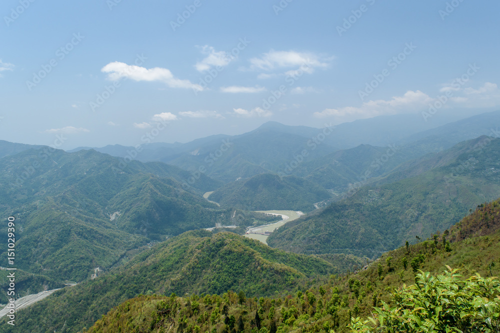 A hilltop view of mountains and blue sky with clouds  on a misty day.
