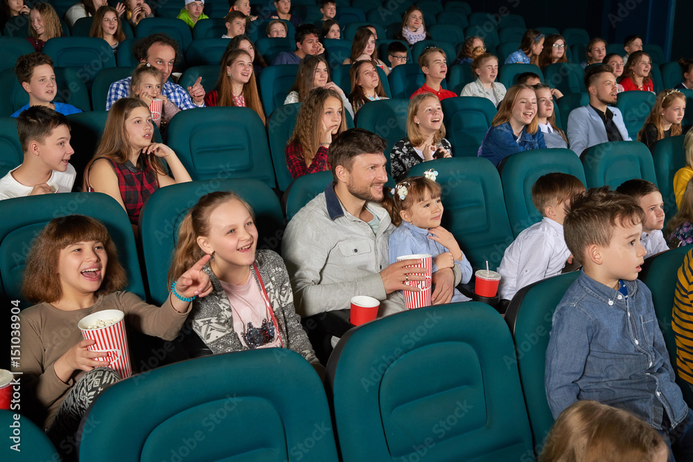 Cinema auditorium full of kids and their parents enjoying premiere of a comedy movie on a weekend happiness positivity leisure emotions excitement amazement entertaining concept. Cinema auditorium full of kids and their parents enjoying premiere of a comedy movie on a weekend happiness positivity leisure emotions excitement amazement entertaining concept.