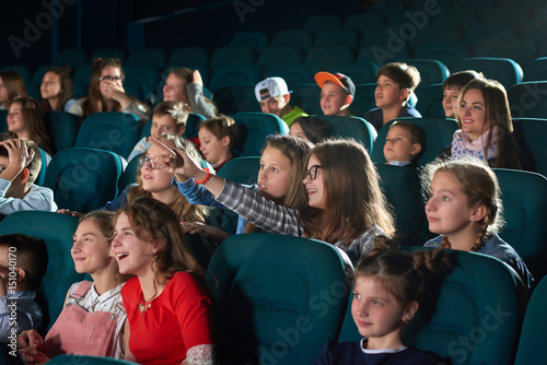 Young girl laughing pointing at the screen while watching a movie at the local cinema children weekend holiday entertainment kids carefree teens fun comedy cartoon concept.