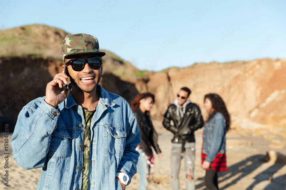 Smiling man talking by phone walking at beach with friends