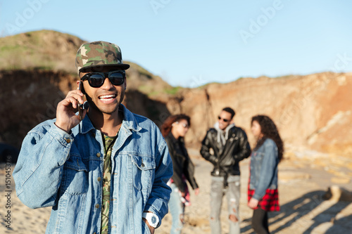 Smiling man talking by phone walking at beach with friends