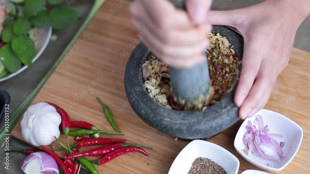 A female hand pounding many kinds of herbs in mortar to make Thai red curry chili paste or Panang.