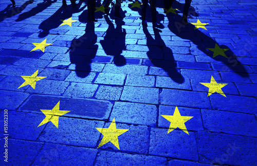 Shadows group of people walking on sunny stone tiled street floor painted with European Union flag.