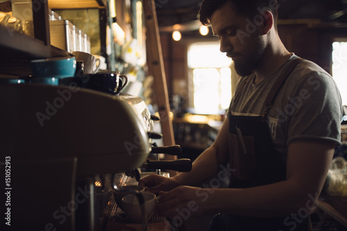 Young male barista preparing drink at coffee machine