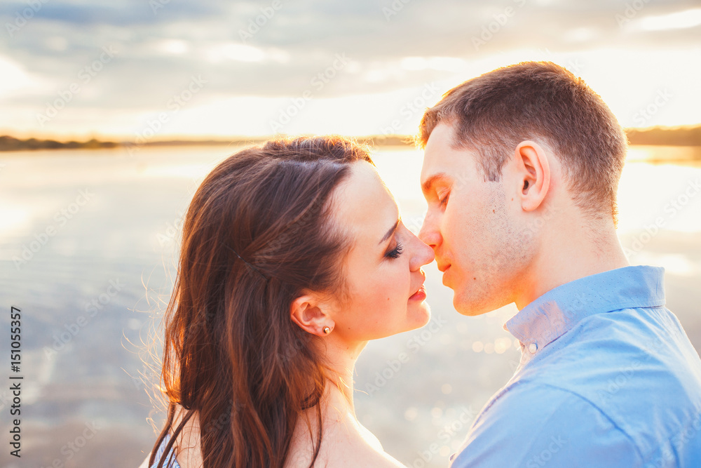 Young beautiful couple in love staying and kissing on the beach on sunset. Soft sunny colors. Young beautiful couple in love staying and kissing on the beach on sunset. Soft sunny colors.