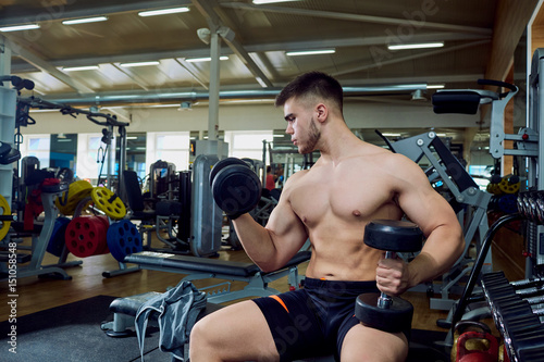 The guy is doing exercises with dumbbells in the gym.