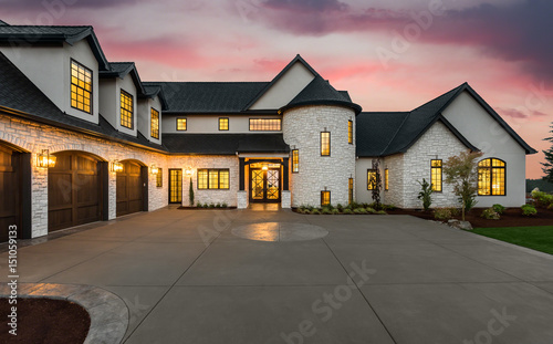 Stunning Luxury Home Exterior at Sunset with Colorful Sky and Expansive Driveway. This Mansion has Three Garages, Turret Style Tower, and Two Floors 