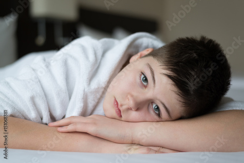 Boy in bathrobe lies in bed in hotel room