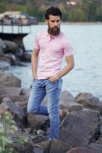 Portrait of a young and handsome  man with a beard in trendy t-short posing on the sea shore. Close up. Sea/beach fashion concept. © elainenadiv