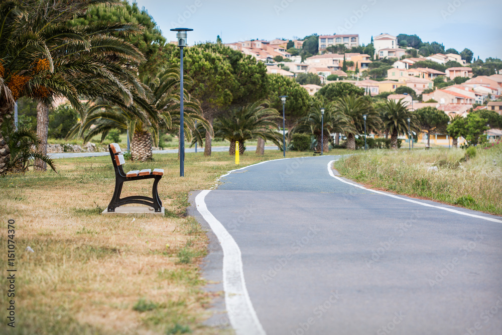 a pedestrian road with palms and benches along it leading to cosy houses on upland