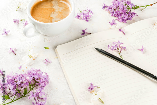 Still life. Spring romantic mood. Breakfast. A cup of coffee, lilac and cherry flowers, a notepad for plans for the day, a pencil. On a white table. Copy space
