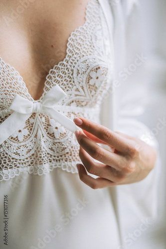 Girl bride tenderly touching bow, dressed in white lace and silk dressing gown in the wedding morning photo