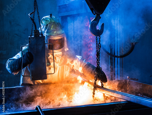 Foundry worker with special protective suit quenching casts in oil bath photo