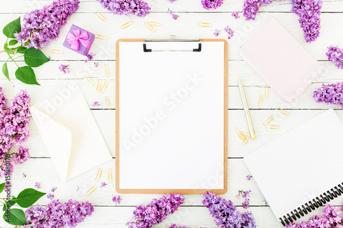 Minimalistic workspace with clipboard, envelope, pen, lilac, box and accessories on white wood background. Flat lay, top view. Beauty blog concept.