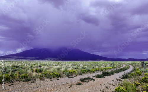 Misty mountain and grassy plain with gravel road and fence, ominous storm clouds, southern Colorado