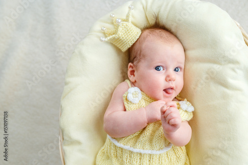 Newborn baby girl lying in a basket with crown and yellow bodysuit