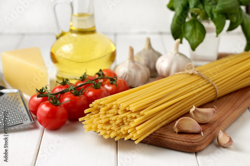 Ingredients for bucatini recipe: pasta, tomatoes, oil, basil, garlic, cheese on white wooden background.