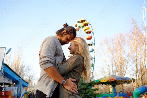 Happy smiling couple in love hug and kiss each other in the amusement park. Sunny warm spring evening
