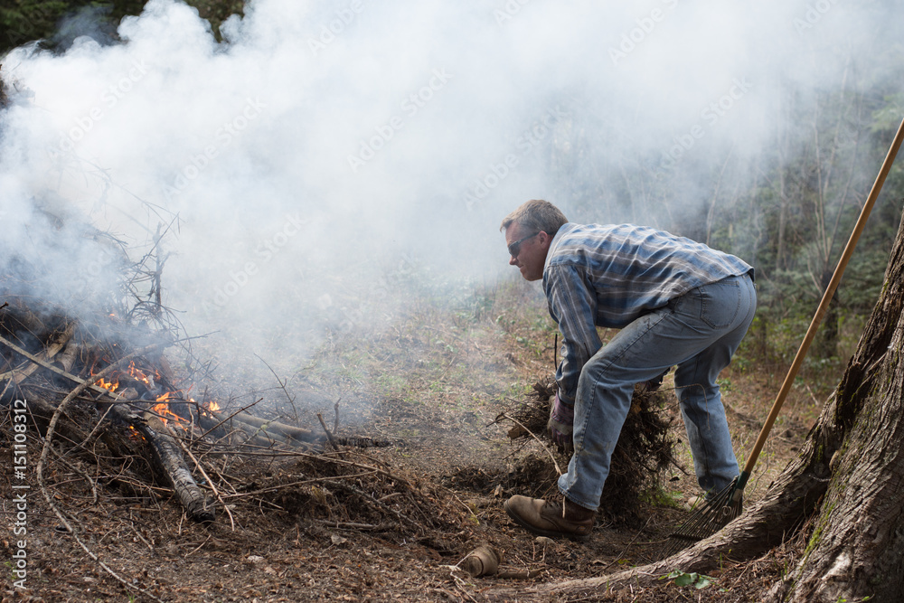 Obraz premium Man doing spring yard work around burn pile.