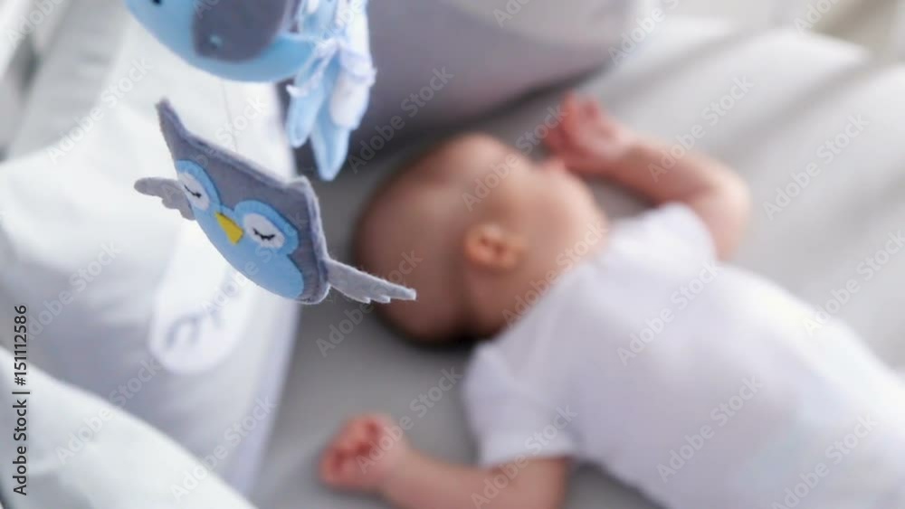 newborn lies in the round white bed with mobile and toys