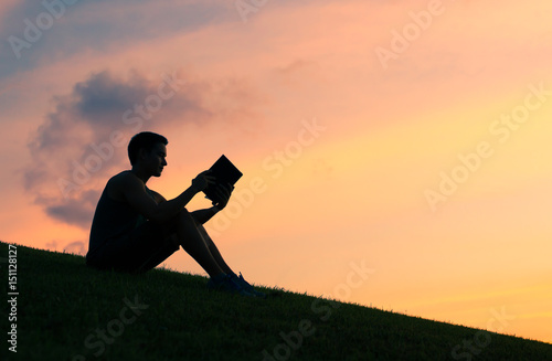 Silhouettes of young man reading a book. 