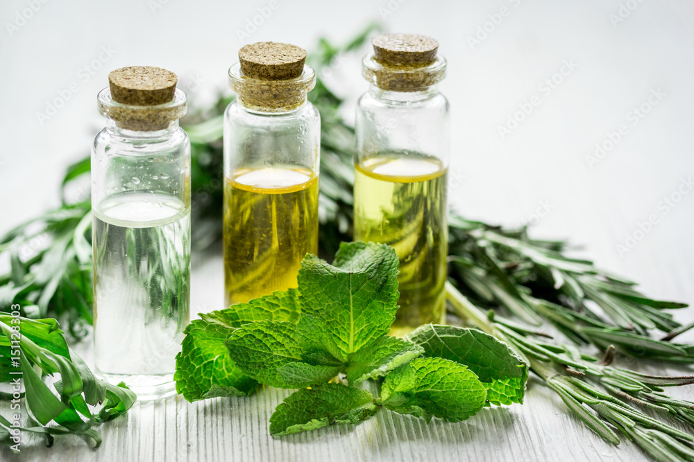 organic oil in bottle with rosemary and mint on light table background organic oil in bottle with rosemary and mint on light table background