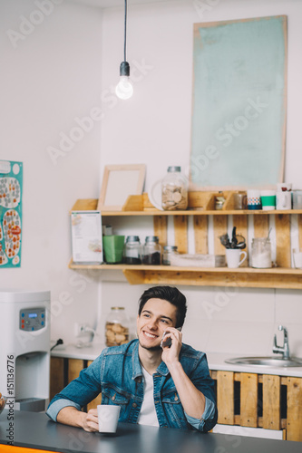 Young Man Relaxing Sitting In Kitchen Talking On Phone