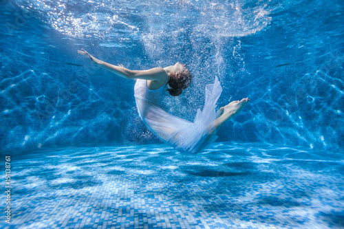Dancing woman under the water in a pool in a white dress, she is like a Rusalka. Surrealistic photography.