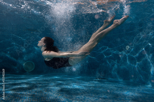 Woman floats under water in the pool, around her vials of air and spot of light.
