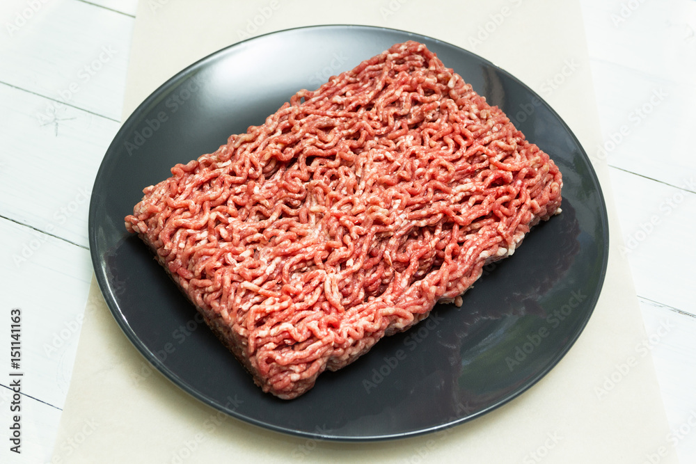 Red forcemeat on a black plate on a white wooden table. Red forcemeat on a black plate on a white wooden table.