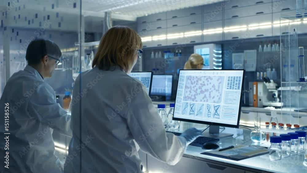 Female and Male Scientists Working on their Computers In Big Modern Laboratory. Various Shelves with Beakers, Chemicals and Different Technical Equipment is Visible. RED Cinema Camera UHD