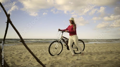 Young long hair woman enjoying windy summer day on sandy beach dunes  Active girl with bicycle on seaside. Female tourist resting near to sea  on fresh air 4K ProR es HQ codec photo