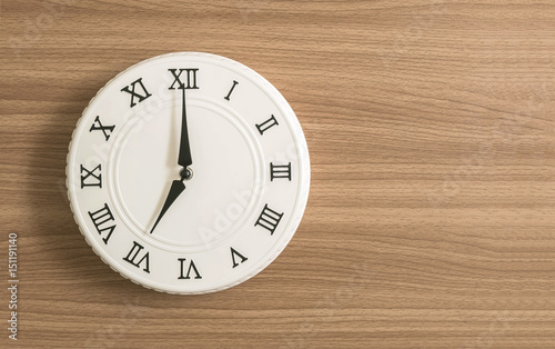 Closeup white clock for decorate in 7 o'clock on wood desk textured background with copy space