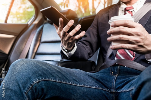 young handsome businessman working in back of car and using a tablet or smart phone