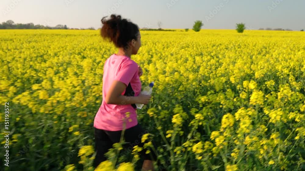 4K video clip of beautiful healthy mixed race African American girl teenager female young woman running or jogging with a bottle of water in field of yellow flowers 4K video clip of beautiful healthy mixed race African American girl teenager female young woman running or jogging with a bottle of water in field of yellow flowers