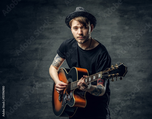 Fashionable hipster blues and jazz acoustic guitar player with tattoos on his arms.