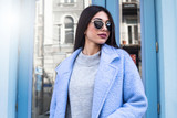 Ultra-fashion concept. young woman of fashion wearing blue coat and posing over blue glass urban background. Street style. businesswoman. outdoors. fashionable accessories.