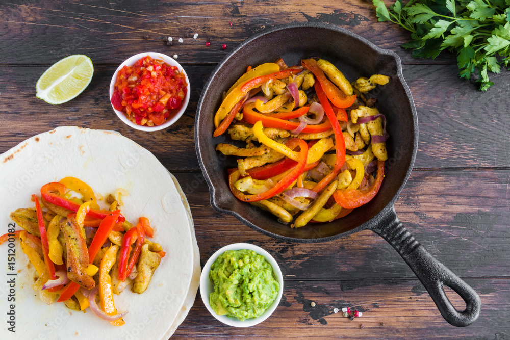 Φωτογραφία Chicken fajitas, fillet roasted with bell peppers and red onion in a black skillet, tortillas and traditional Mexican sauces salsa and guacamole