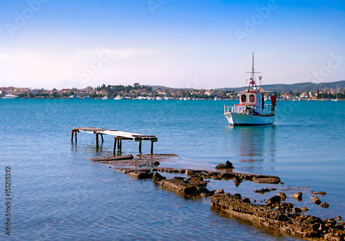 Destroyed pier and white small wooden fishing boat. View of Porto Heli town  in the background. Greece photo