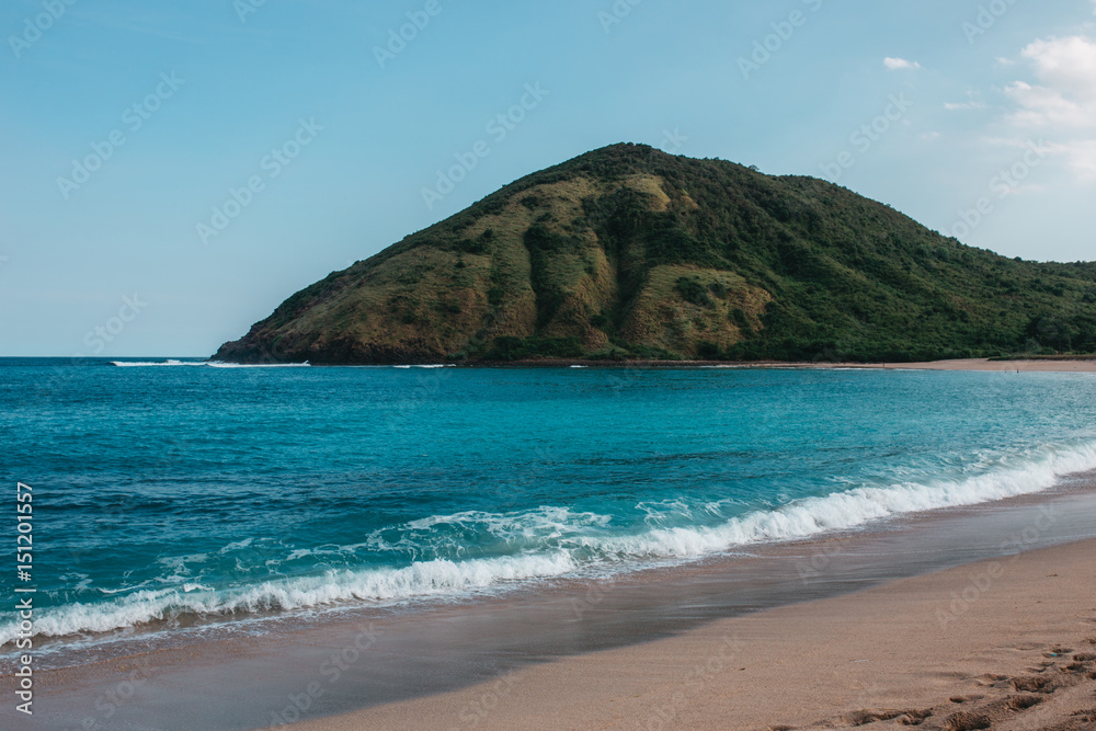 Landscape with a tropical beach with green hills, rocks on the background, water is azure and sand is white, Indonesia, Lombok