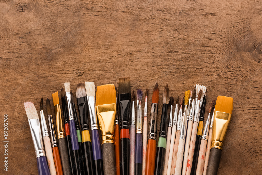 Fototapeta premium Close-up top view of various paintbrushes collection on brown wooden table