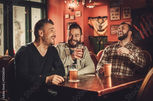 Cheerful old friends having fun and drinking draft beer in pub.