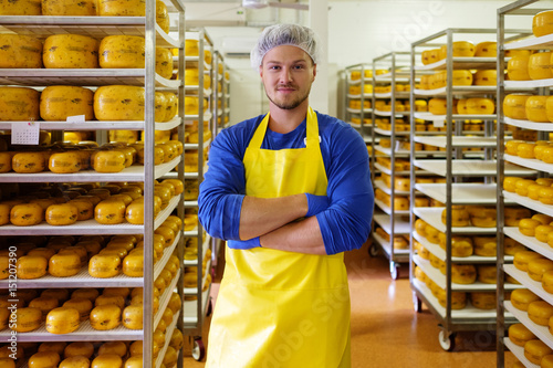 Handsome cheesemaker is checking cheeses in his workshop storage.